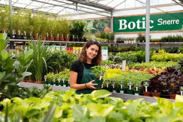 Employée souriante avec plante dans serre de Botanic Suresne entourée de verdure abondante