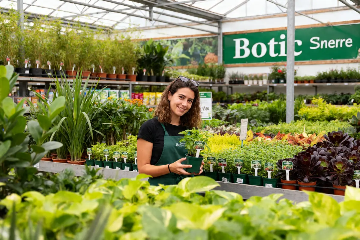 Employée souriante avec plante dans serre de Botanic Suresne entourée de verdure abondante