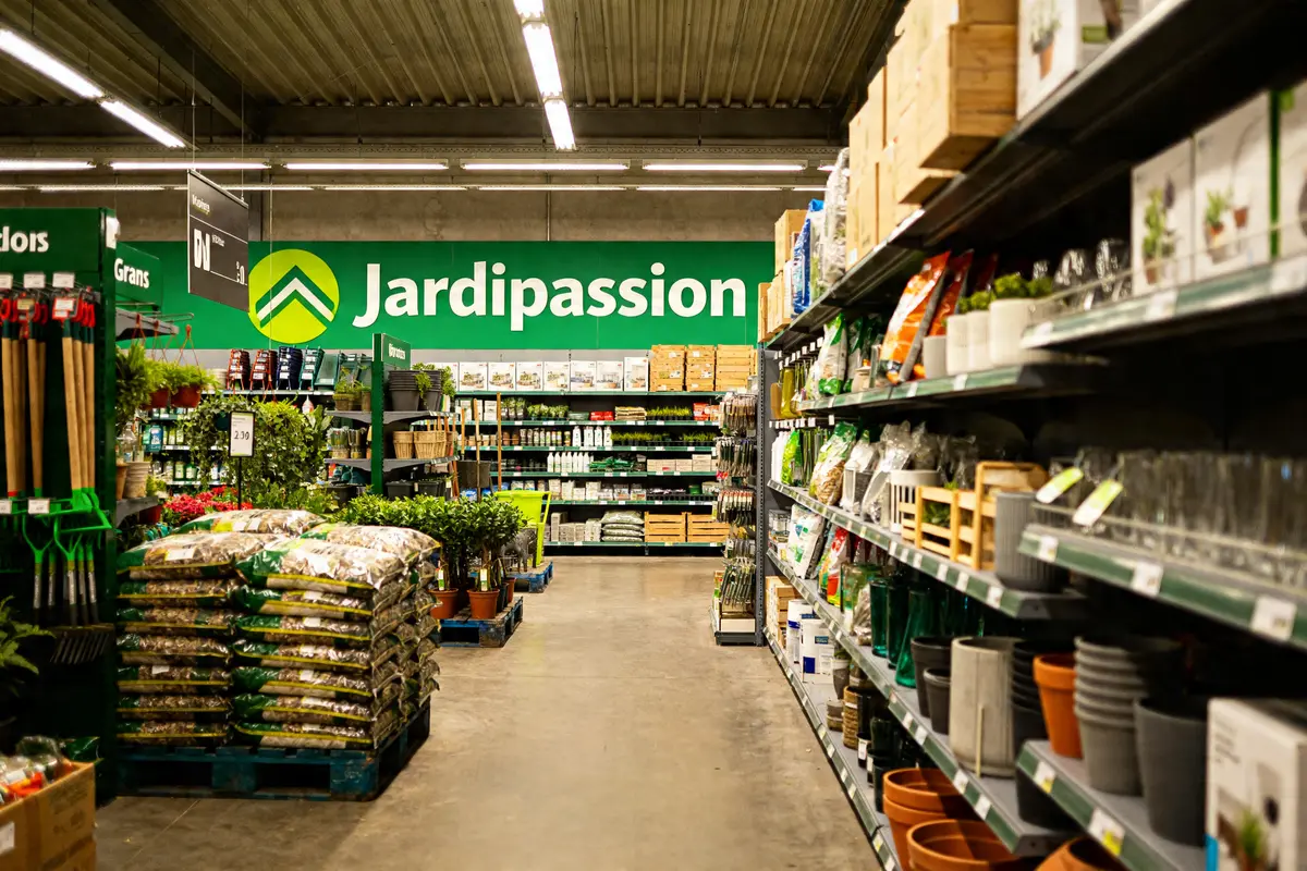 Allée centrale du magasin Jardipassion Grans avec outils de jardinage et végétaux en exposition