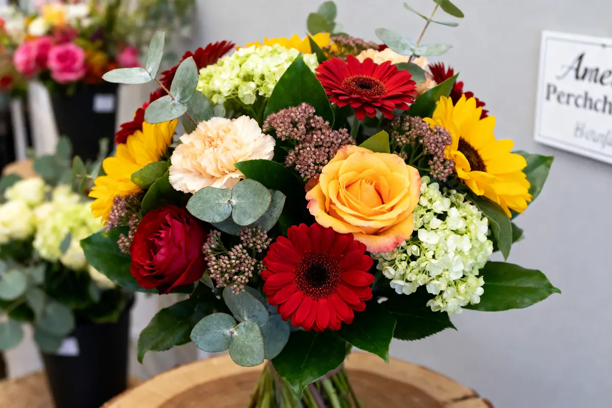 Bouquet coloré de roses, tournesols, gerberas chez Angele Fleurs sur un présentoir bois