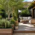 Terrasse en bois avec salon extérieur, canapés, table basse et plantes dans un jardin verdoyant et ombragé.
